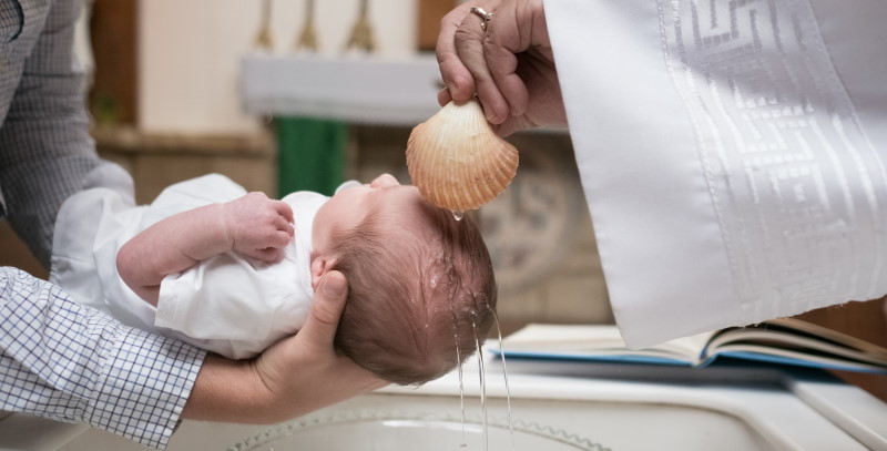 Μωρό στα χέρια μια γυναίκας λαμβάνει άγιο νερό από κοχύλι