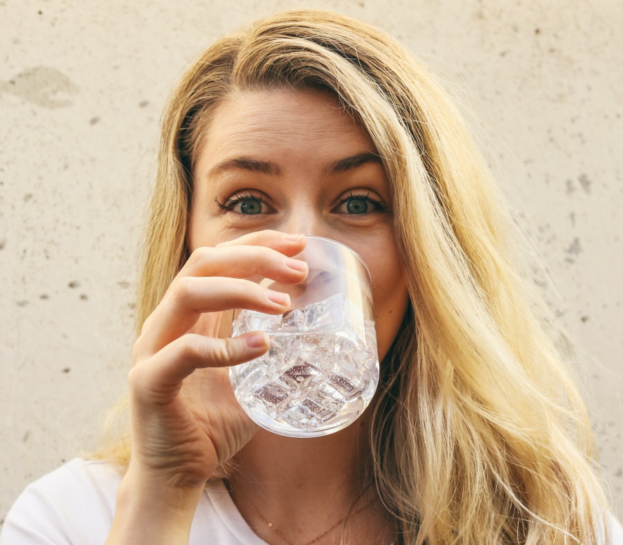 Γυναίκα με ένα ποτήρι νερό μπροστά στο πρόσωπό της, πίνει νερό